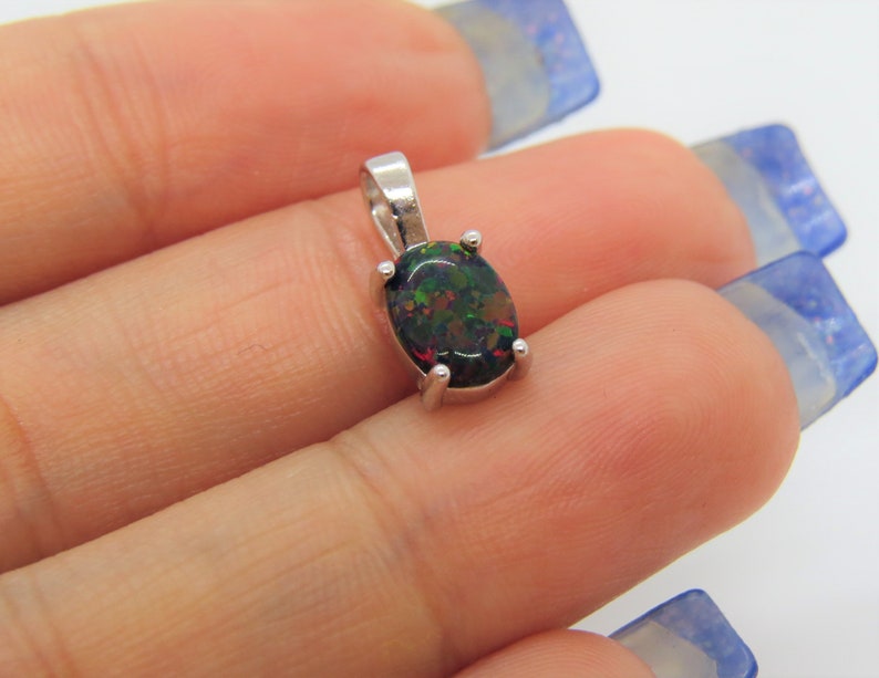 Puede incluir: Un colgante de plata con una piedra preciosa de &oacute;palo negro. El &oacute;palo tiene destellos de color verde, rojo y marr&oacute;n.