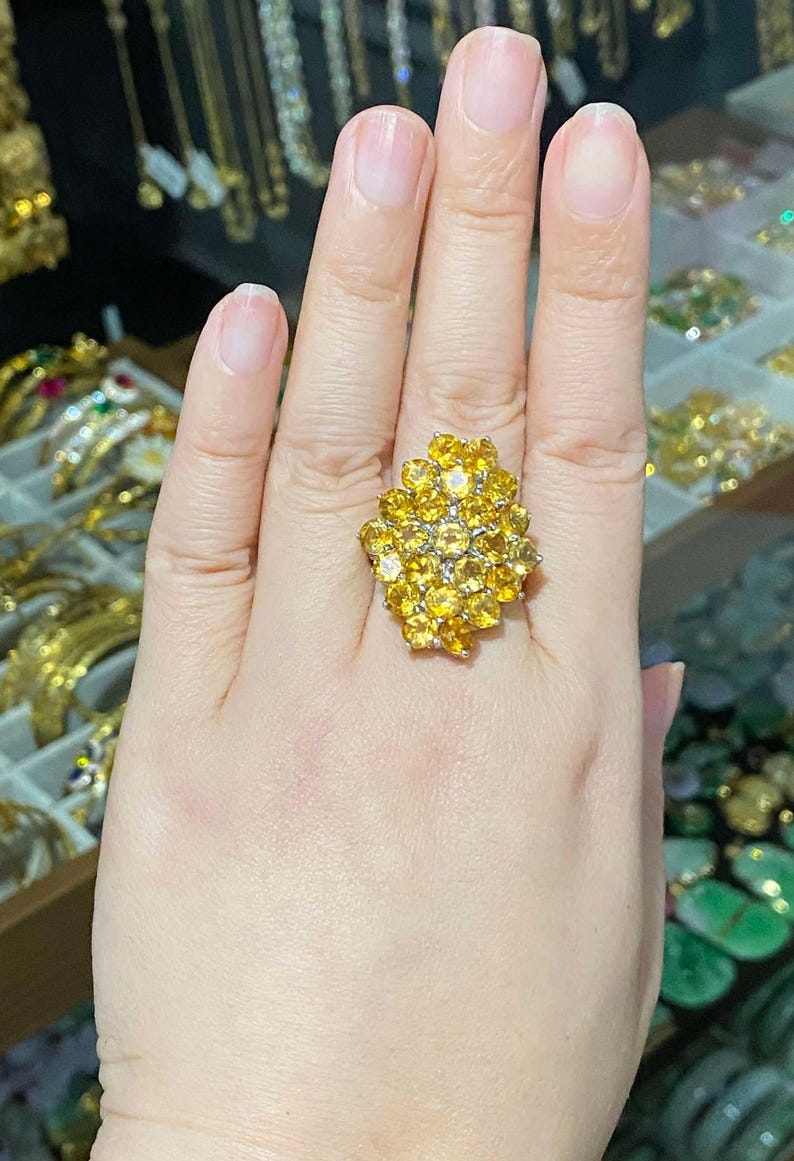 May include: A gold ring with a cluster of yellow gemstones. The ring is worn on the index finger of a hand.