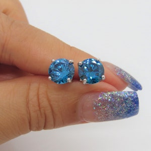 Puede incluir: Un par de pendientes de bot&oacute;n de plata con grandes piedras azules redondas.