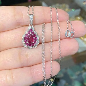 May include: A silver chain necklace with a teardrop-shaped pendant featuring a large oval ruby surrounded by smaller rubies and diamonds.