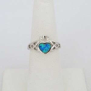 K&ouml;nnte beinhalten: Ein silberner Ring mit einem keltischen Knoten, einem blauen Opal in Herzform und einer Krone obenauf.