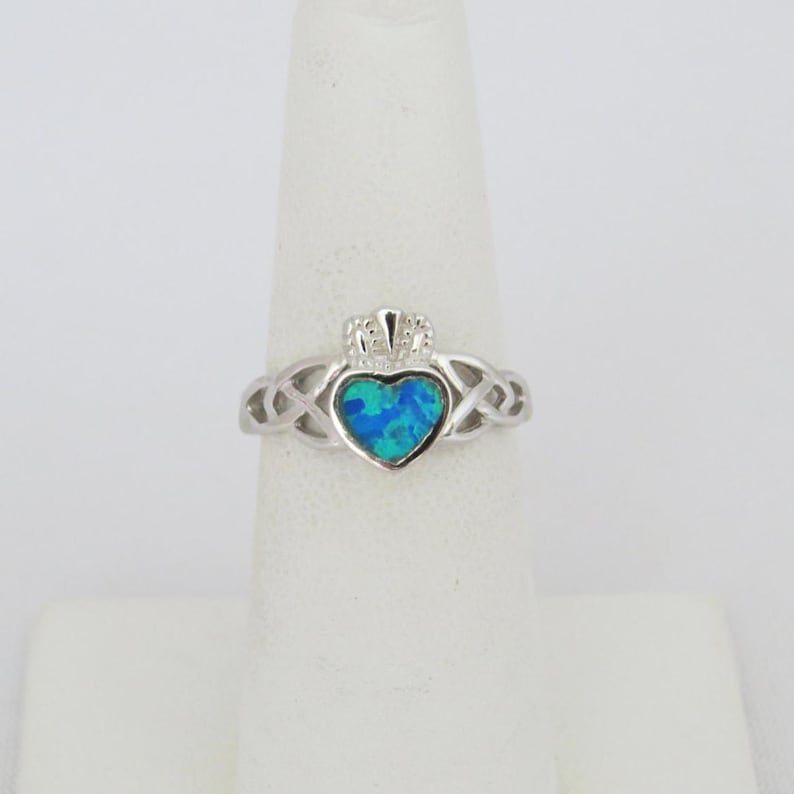 K&ouml;nnte beinhalten: Ein silberner Ring mit einem keltischen Knoten, einem blauen Opal in Herzform und einer Krone obenauf.