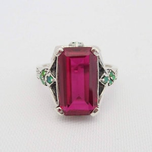 May include: A silver ring with a large, rectangular, pink gemstone surrounded by smaller green gemstones.