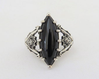 May include: A silver ring with a black onyx marquise-shaped gemstone set in a detailed floral design.