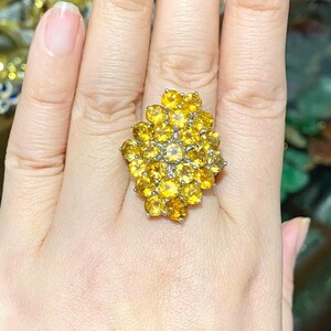 May include: A large, yellow gemstone ring with a cluster of round stones set in a silver band.