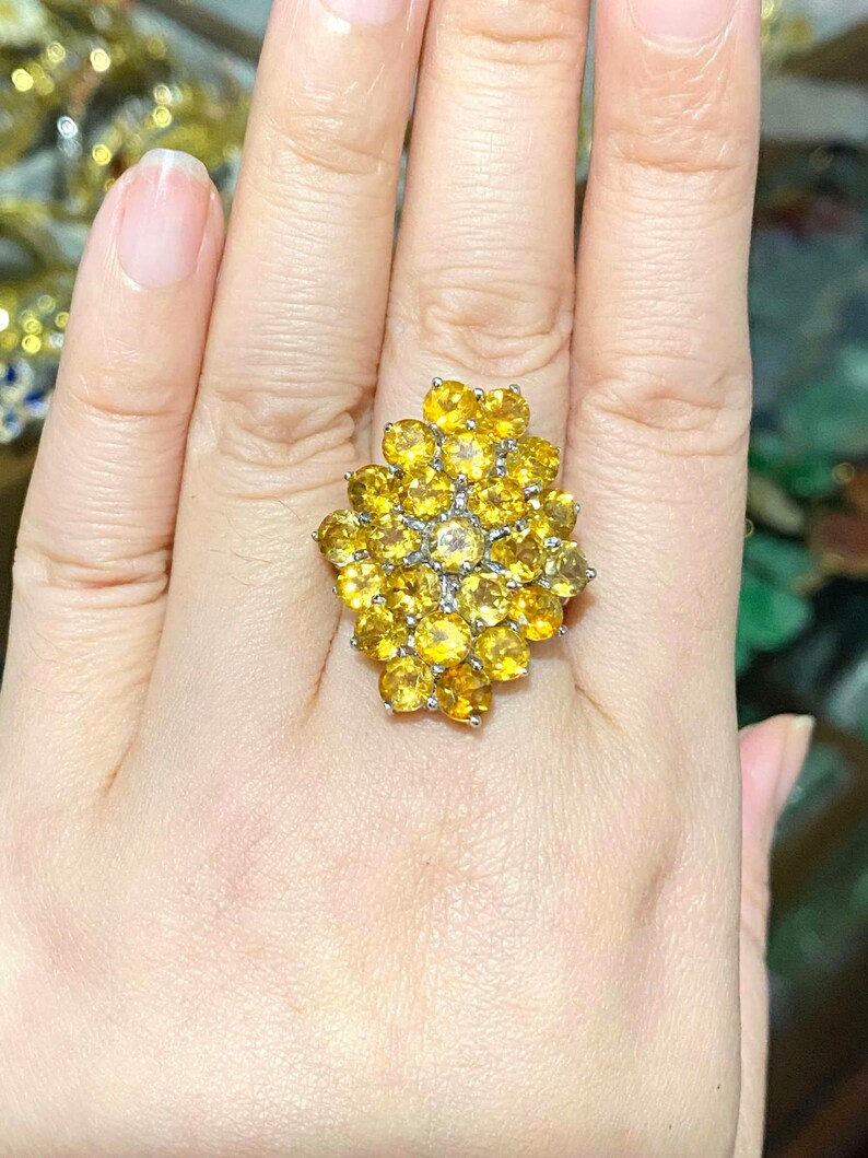 May include: A large, yellow gemstone ring with a cluster of round stones set in a silver band.