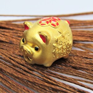 May include: A small golden pig figurine with red and white accents. The pig has Chinese characters on its side and a flower design on its back.