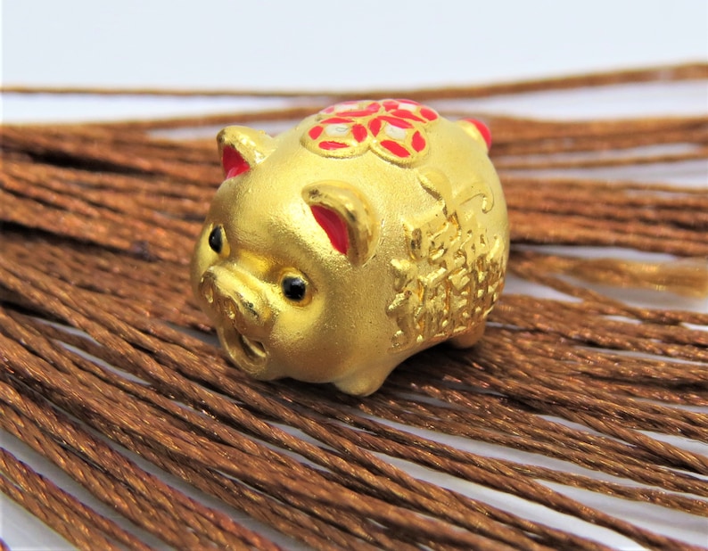May include: A small golden pig figurine with red and white accents. The pig has Chinese characters on its side and a flower design on its back.