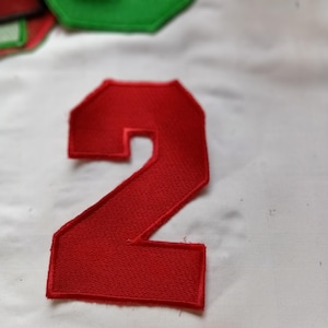 Può includere: Una toppa ricamata rossa a forma di numero due con un bordo cucito spesso. La toppa presenta una costruzione in filo denso e testurizzato e un colore rosso solido e audace su tutta la cifra, progettata per l'applicazione su tessuti.
