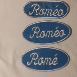 Può includere: Tre toppe blu ricamate con il nome "Roméo" in corsivo bianco. Le toppe sono ovali e rettangolari, con un bordo bianco. Le toppe sono probabilmente per abbigliamento o accessori.