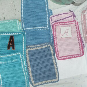 Könnte beinhalten: Eine Sammlung rechteckiger Häkeltaschen in verschiedenen Farben wie Türkis, Blau, Rosa und Magenta. Einige Taschen haben einen weißen Rand, einen schwarzen Buchstaben A-Aufnäher oder gestickten Text und sind flach angeordnet.