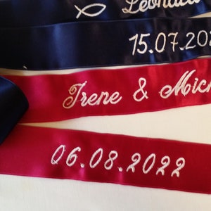 May include: Navy blue and red satin ribbons with white embroidered text. The ribbons feature names and dates, including "Irene & Michael" and "06.08.2022". These ribbons are suitable for a special occasion, such as a wedding or anniversary.