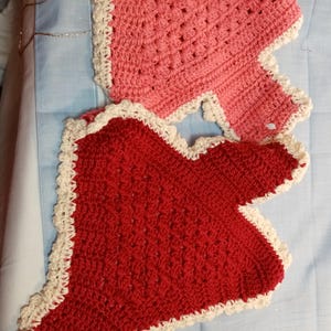 Könnte beinhalten: Zwei gehäkelte herzförmige Decken, eine rote und eine rosa, mit weißer Häkelborte.