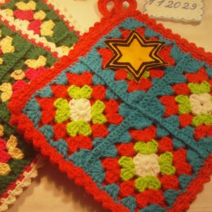 May include: Two handmade crochet potholders. One is green with red, white, and yellow floral patterns, and the other is blue, red, and white with a yellow star. The potholders are square with scalloped edges.