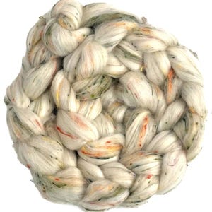 Puede incluir: Un grueso manojo trenzado de fibra de mecha color blanco roto con sutiles motas dispersas de color naranja, amarillo y verde por todo el material suave y texturizado. La fibra está enrollada en una forma circular densa con hebras visibles.
