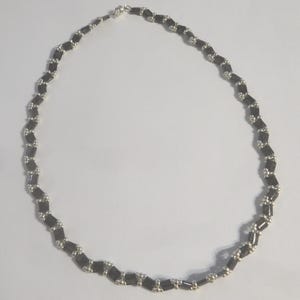 Puede incluir: Un collar de cuentas negras y plateadas con un patrón geométrico.