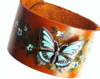 May include: A brown leather cuff bracelet with a painted floral design and a turquoise butterfly charm.