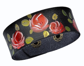 May include: Black leather cuff bracelet hand-painted with red roses, green leaves, and yellow accents. The bracelet features a snap closure with two antique brass-colored snaps. A unique floral accessory.