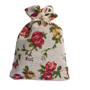 May include: A small, white drawstring bag with a floral pattern. The bag is made of a linen-like fabric and features red, pink, and yellow roses.