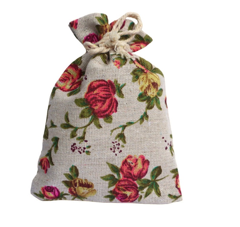 May include: A small, white drawstring bag with a floral pattern. The bag is made of a linen-like fabric and features red, pink, and yellow roses.