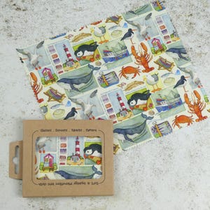 May include: A brown cardboard box with a clear plastic window showing a microfiber cleaning cloth with a colorful pattern of seagulls, lighthouses, puffins, whales, and crabs. The text on the box reads "Glasses - Screens - Tablets - Cameras - Self Adhesive - Machine Washable - Air Dries to a Soft Finish".