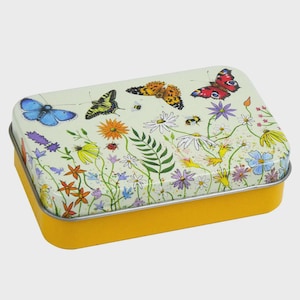 Könnte beinhalten: Eine rechteckige gelbe Dose mit einem Deckel, der mit Schmetterlingen, Bienen und Wildblumen verziert ist. Der Deckel hat ein Gartenszenen-Design. Die Dose hat einen silbernen Rand und einen gelben Boden.
