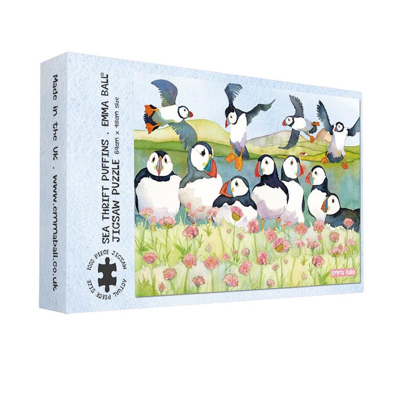 May include: A 1000-piece jigsaw puzzle featuring a watercolor illustration of puffins in a coastal scene. The puzzle box displays the text "SEA THRIFT PUFFINS" and measures 64cm x 48cm. The puzzle is made in the UK.