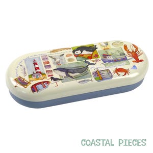 May include: A white and blue oval-shaped glasses case with a colorful illustration of a lighthouse, a whale, a puffin, a crab, and other sea life. The text "Pieces of the ocean found on the shoreline..." is printed on the case.