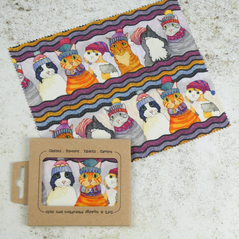 May include: A microfiber cleaning cloth with a colorful pattern of cats wearing winter hats and scarves. The cloth is packaged in a cardboard box with the text "Glasses - Screens - Tablets - Camera" and "Soft & Absorbent Microfibre Lens Cloth".