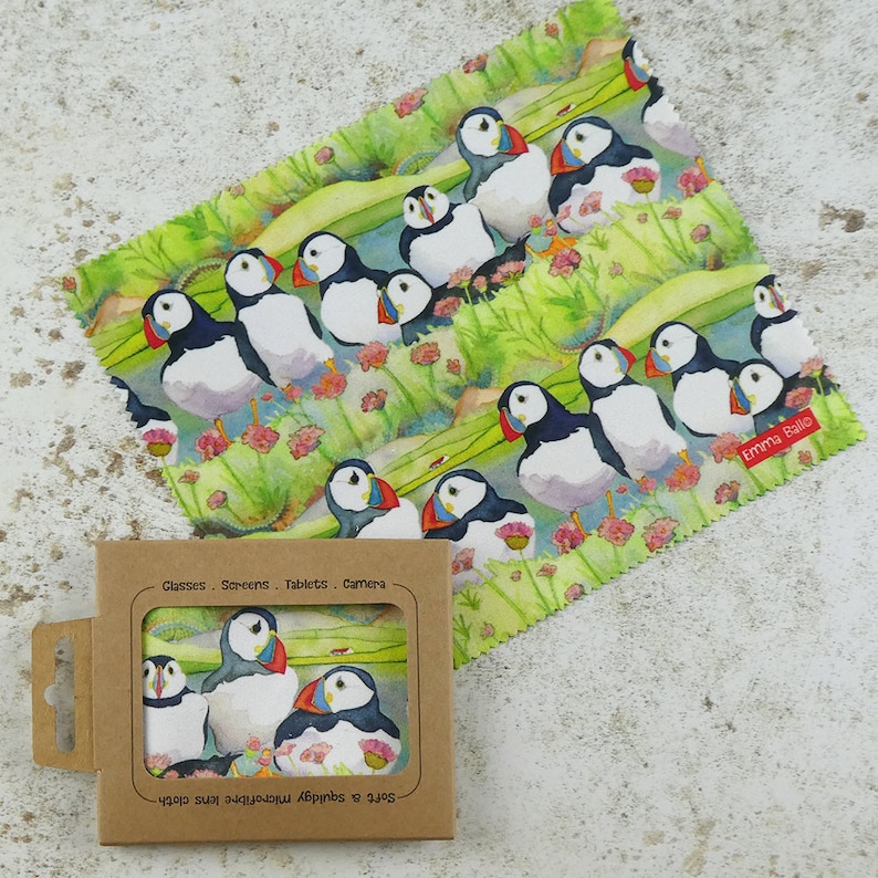 May include: A microfiber cleaning cloth with a colorful design of puffins on a green background. The cloth is packaged in a brown box with the text "Soft & Absorbent Microfibre Lens Cloth" and "Glasses - Screens - Tablets - Camera".