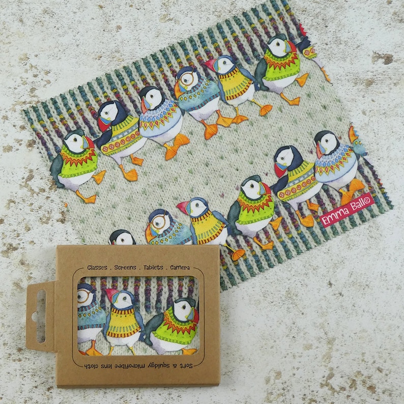 May include: A set of four microfiber cleaning cloths featuring a whimsical design of puffins wearing colorful sweaters. The cloths are packaged in a brown cardboard box with the text "Glasses, Screens, Tablets, Camera" and "Soft & squidgy microfiber lens cloth" printed on it. The cloths are ideal for cleaning glasses, screens, tablets, and cameras.