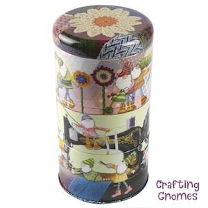 May include: A cylindrical metal tin with a colorful design featuring gnomes and sewing-themed imagery. The tin has a patchwork design with a large flower on the lid. The text "Crafting Gnomes" is printed on the bottom of the tin.