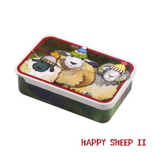 May include: A rectangular lunchbox with a red-edged lid, showcasing a watercolour illustration of three sheep in colourful knitted hats. The lunchbox has a white rim and a green and purple base. The text "HAPPY SHEEP II" is printed in red.