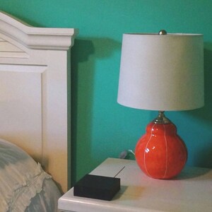 Handmade coral red ceramic table lamp with white stripes on table, topped with white linen shade