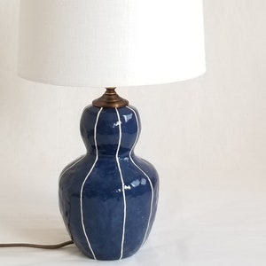 Bedside table lamp in dark blue with thin white stripes. Topped with a white linen shade and matching finial