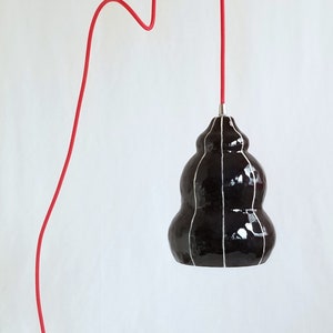 black ceramic pendant light with thin white stripes hangs from a red 15' plugin cord
