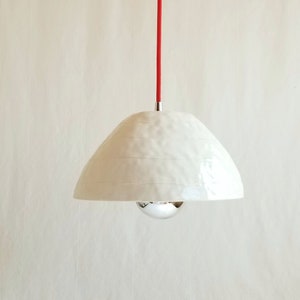 May include: White ceramic pendant light with a textured surface and a red cord. The light fixture has a round, chrome-plated bulb.