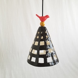 May include: A black ceramic pendant light with a geometric pattern and a red bird perched on top. The bird has a yellow bead for a body.