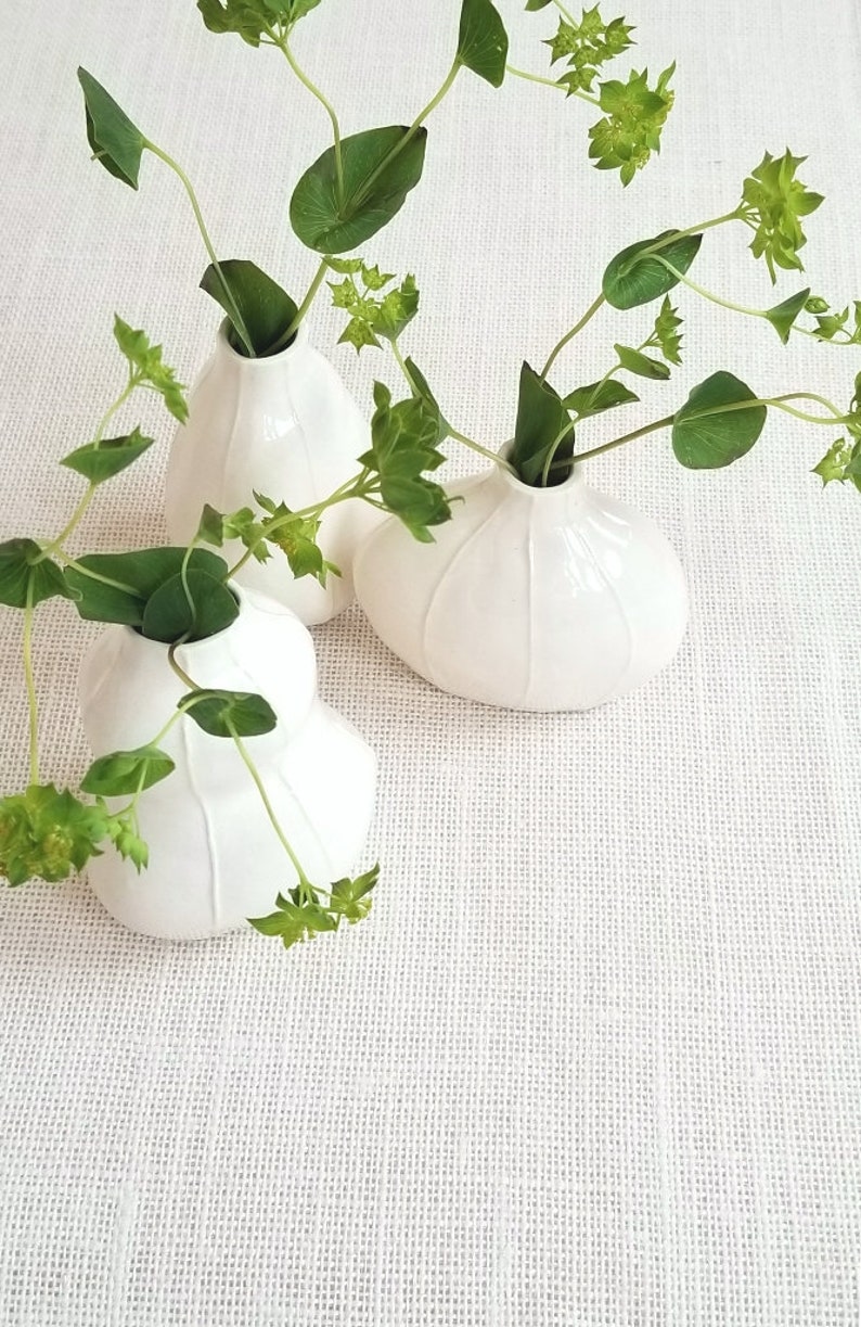 Set of 3 white ceramic bud vases handmade  with thin, raised white stripes. Shown with green foliage