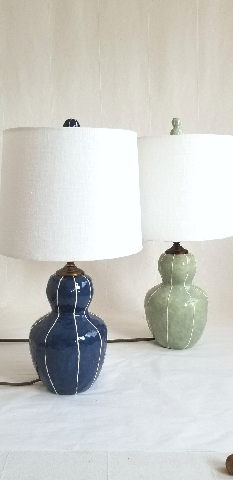 2 Bedside table lamps in dark blue & Celadon with thin white stripes. Topped with white linen shades and matching finials