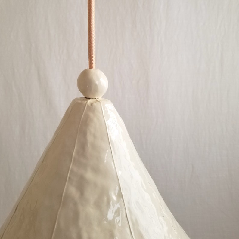 Detail of large, 15" diameter, white ceramic cone pendant light with bead detail. Hangs from copper-pink cord. Handmade in clay with thin, raised white stripes