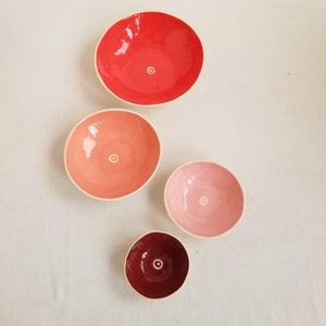 small, handmade ceramic bowls in red, peach, pink& maroon.
white circle and dot in bottom of each
