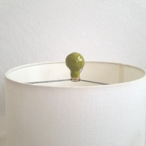 May include: A white lampshade with a green ceramic finial on top.