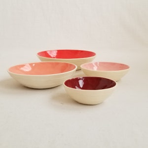 small, handmade ceramic bowls in red, peach, pink& maroon. Raised white stripes on outside