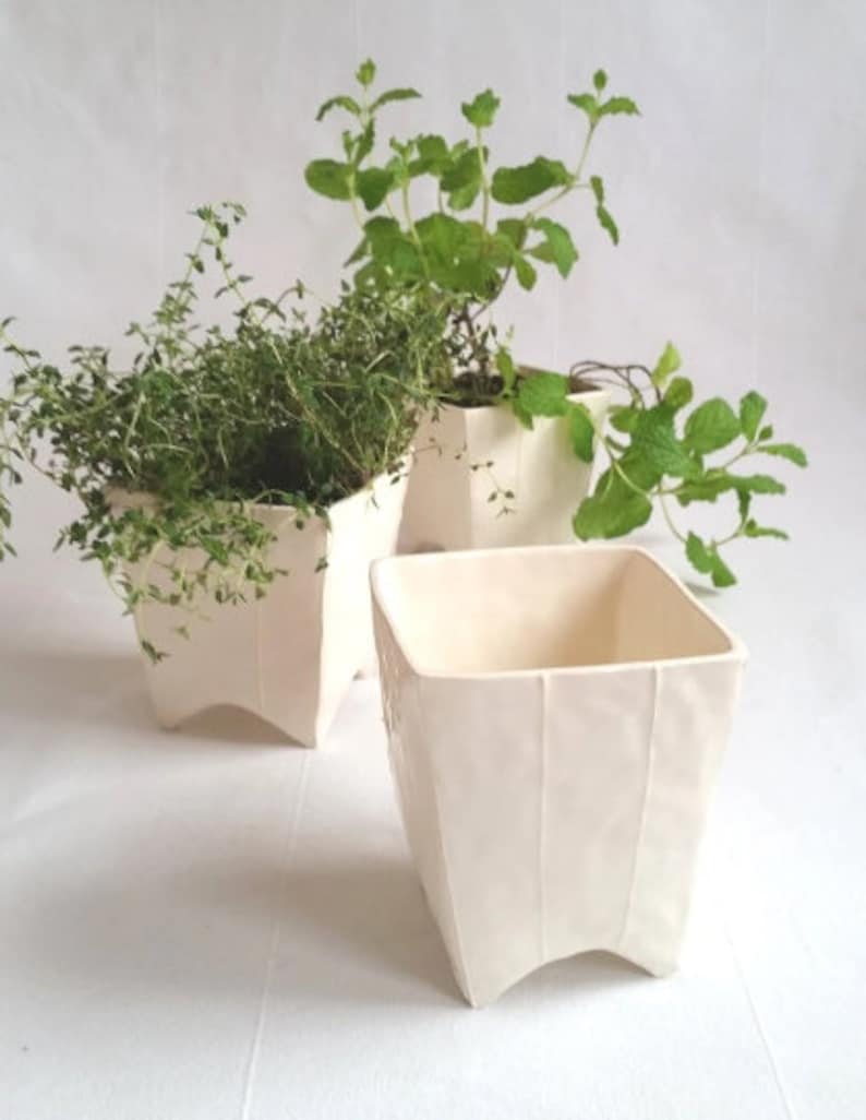 3 Small square ceramic planters with 4 pointed feet. Shown in white with and without potted plants