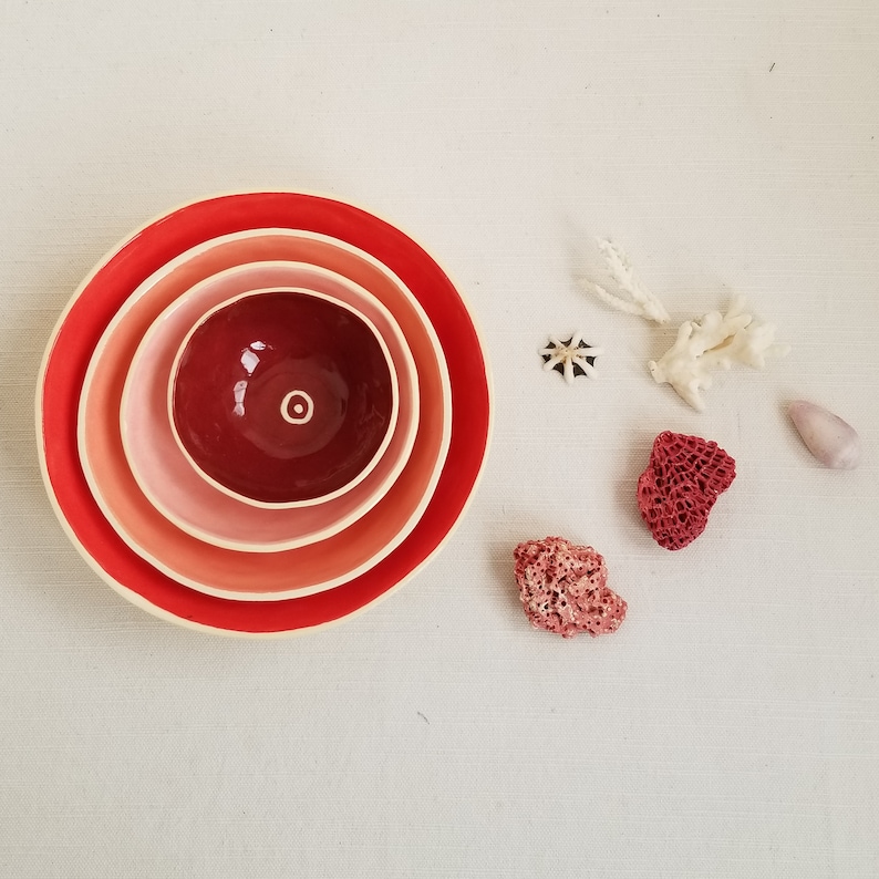 small, ceramic bowls in shades of red, nesting one inside the other with coral
