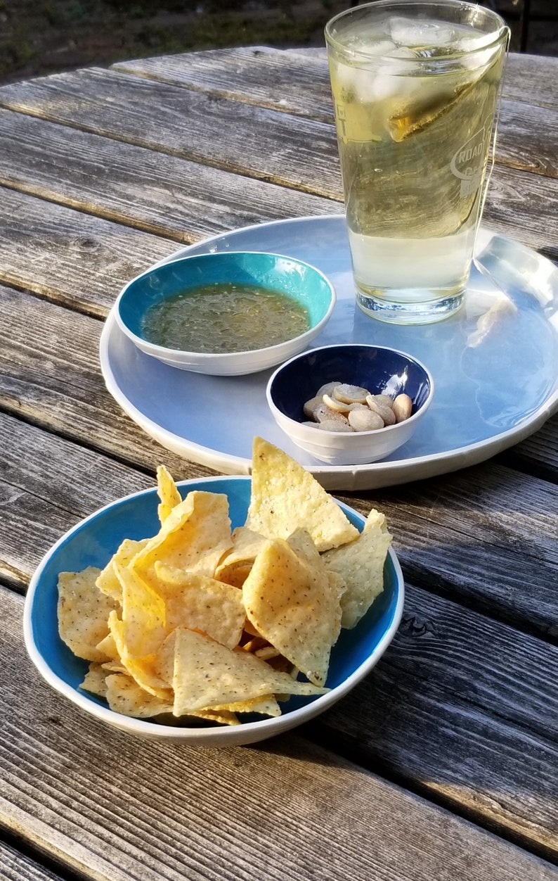 set of 4 nesting bowls in different shades of blue shown in garden setting with chips and dip