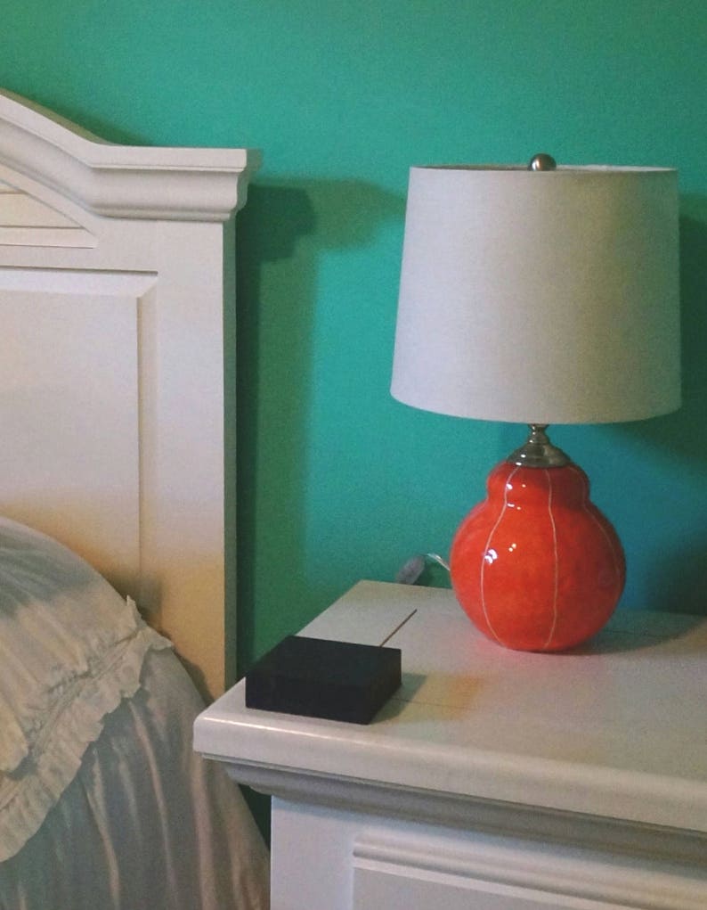 Handmade coral red ceramic table lamp with white stripes on table, topped with white linen shade