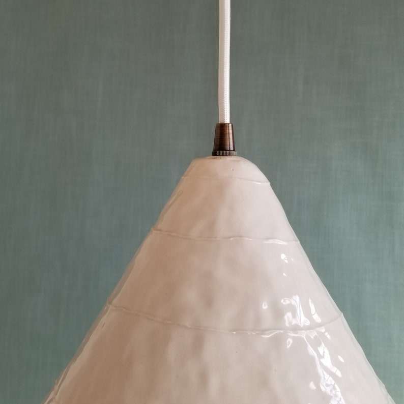 Detail of large, 15" diameter, white ceramic cone pendant light. Hangs from white cord with bronze hardware