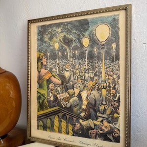 May include: Framed vintage print depicting an open-air concert scene. The artwork features a singer in a green dress, an orchestra, and an audience under streetlights. The print is in a gold-colored frame.
